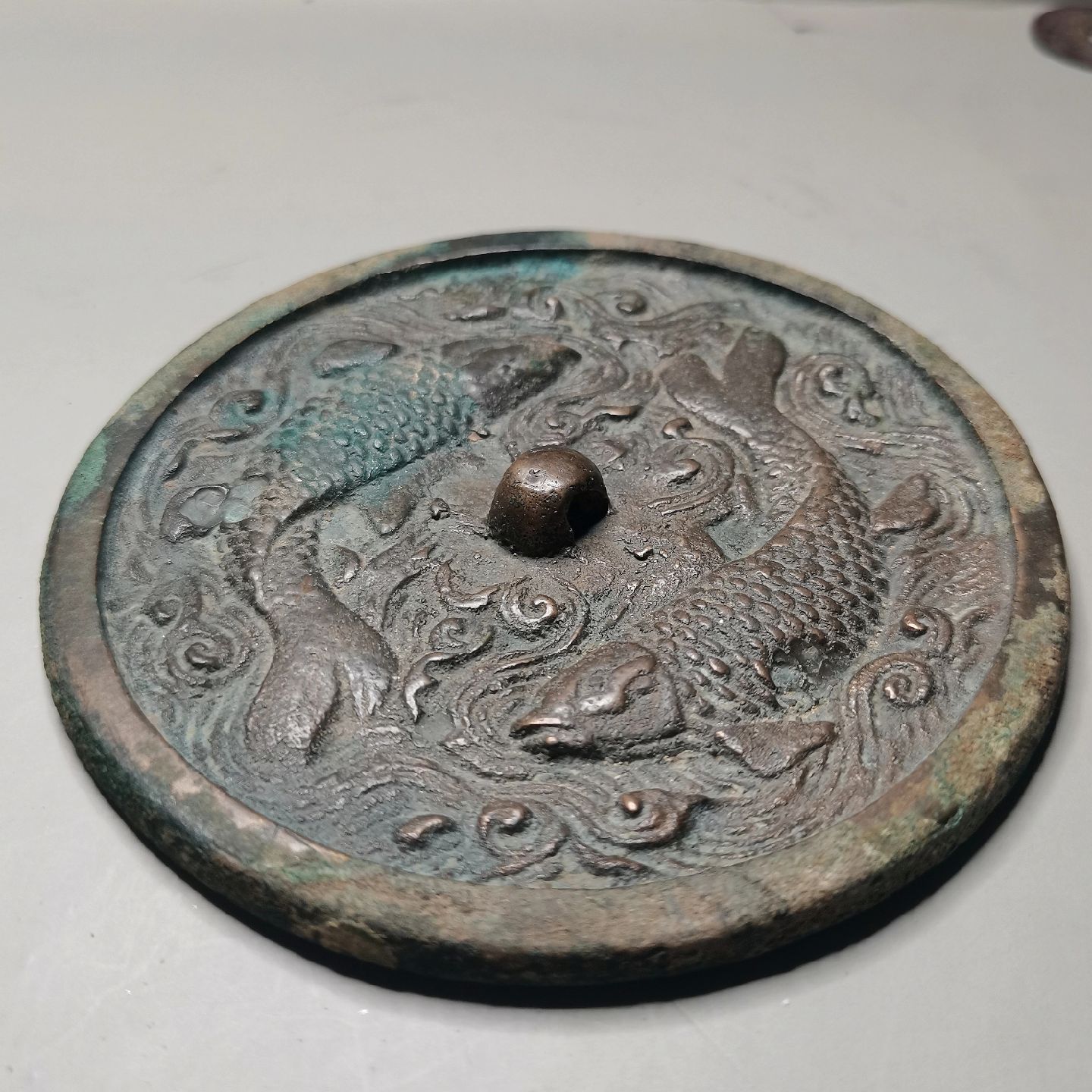 这面双鱼铜镜为圆形,平顶圆钮,镜背面布满了动感的水波纹,与水草纹